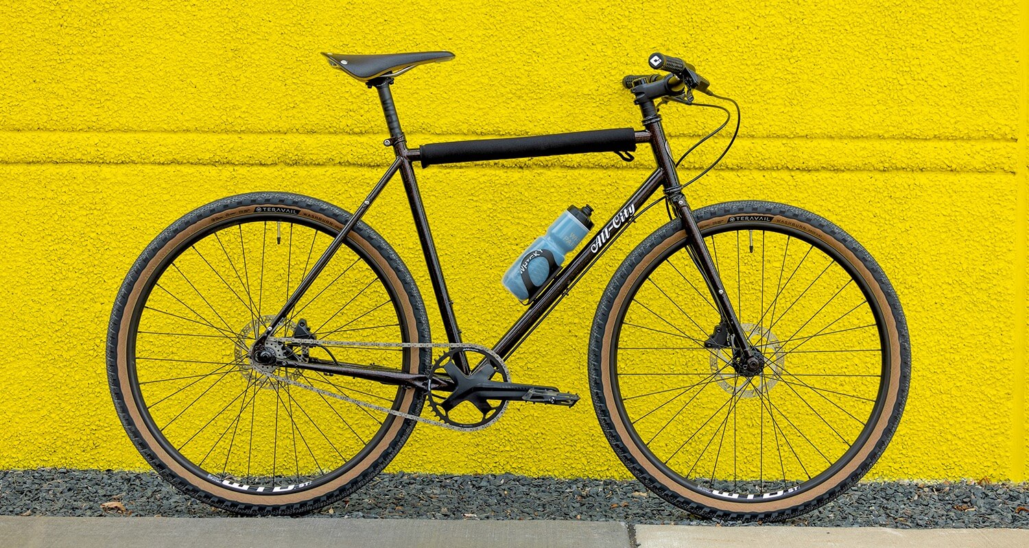 Complete side view of a black bike with a Scully bar next to a yellow concrete wall.