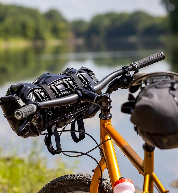 A bike with a Whisky Scully handlebar is parked next to a lake. A pack is attached to the bars.