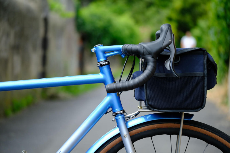 Closeup profile image of the drop bar handlebar and handlebar bag on a Victore Cycles blue randonneur bike.
